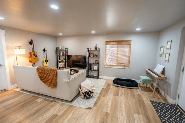 Spacious room featuring light wood-finish flooring, recessed lighting, and a window with natural woven blinds