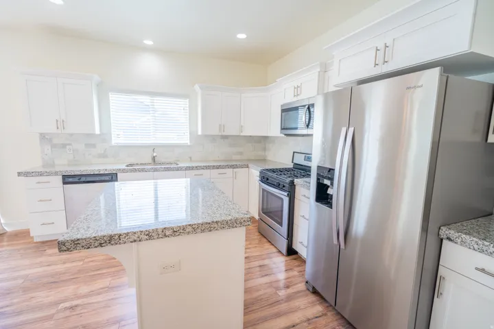 Kitchen featuring white shaker cabinetry, stainless steel appliances, speckled stone countertops, a tile backsplash, and wood-finish flooring