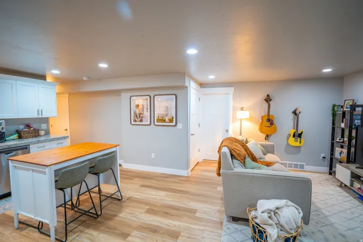 Open-concept living space featuring wood-finish flooring, recessed lighting, a kitchen island with seating, white shaker cabinetry, and granite-style countertops