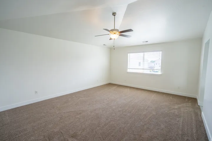 Spacious room featuring neutral carpeting, white walls, and a ceiling fan with light fixture