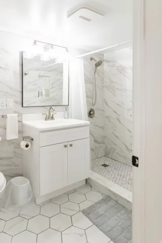 Bathroom featuring a walk-in shower with hexagonal floor tile, marble-look wall tile, a white vanity with storage, and a contemporary light fixture