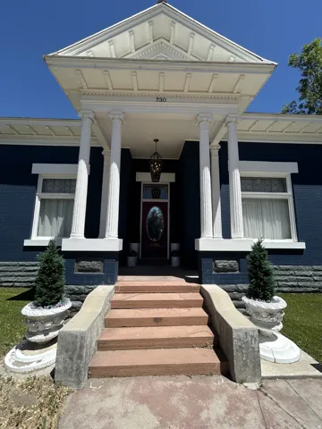 Front facade featuring a classic columned portico, dark blue exterior siding, and a red entry door with an oval glass insert