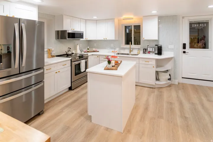 Bright kitchen featuring white cabinetry, light wood-finish flooring, stainless steel appliances, a center island, and a tile backsplash