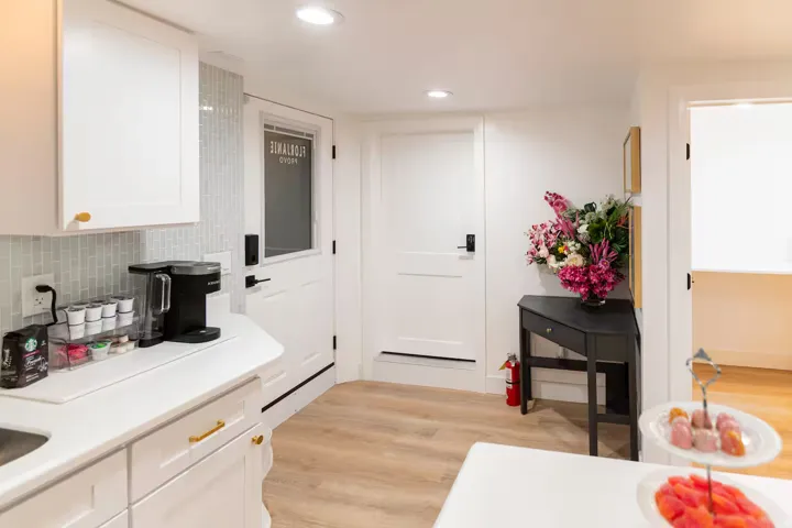Modern kitchen area featuring white cabinetry with gold-tone hardware, a light-toned tile backsplash, and light wood-finish flooring