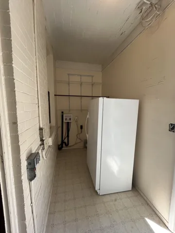 Utility area featuring light-toned flooring, white painted brick wall, and wall-mounted shelving