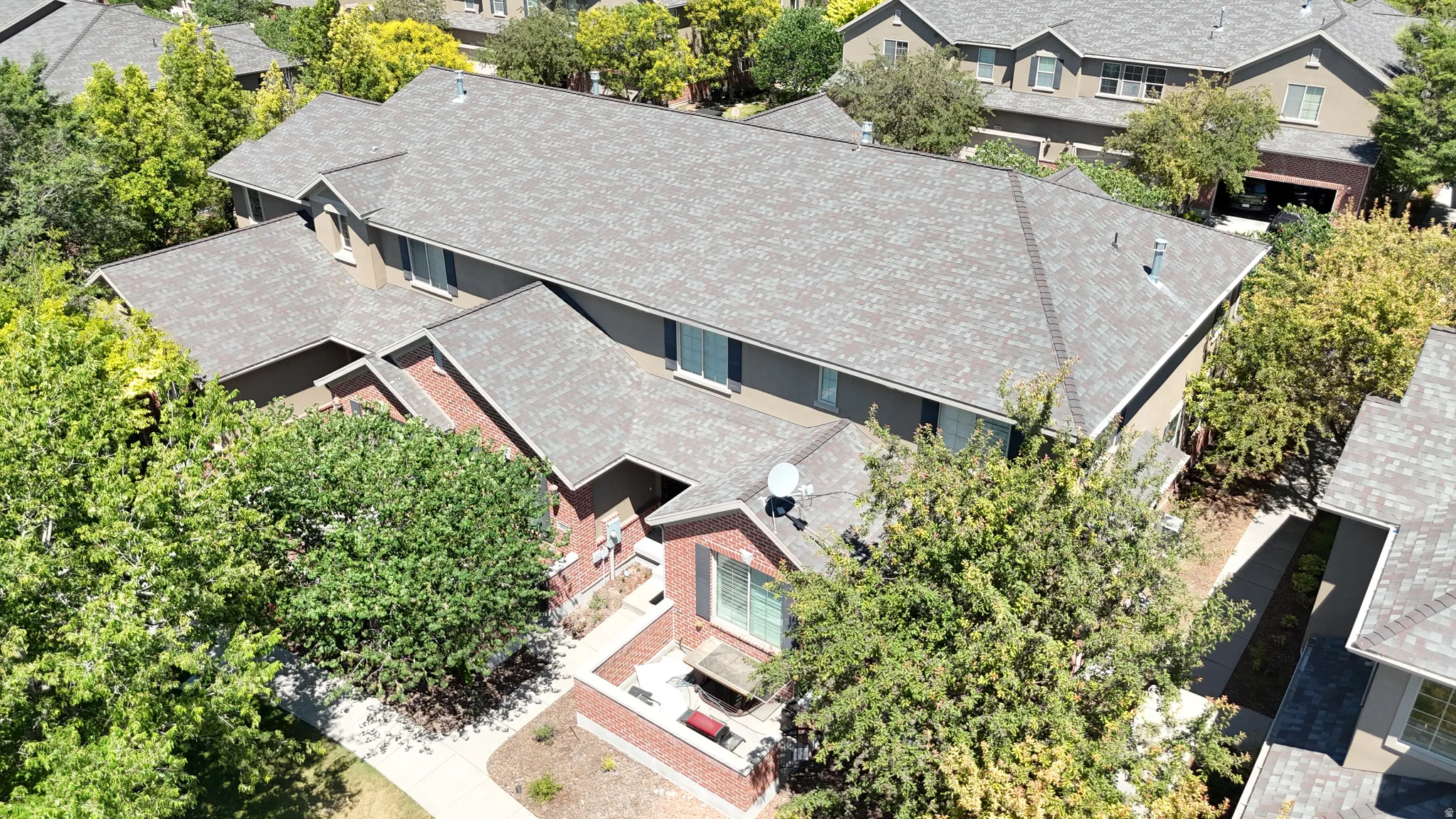 Stucco and brick facade residence with a gray shingle roof, surrounded by mature trees