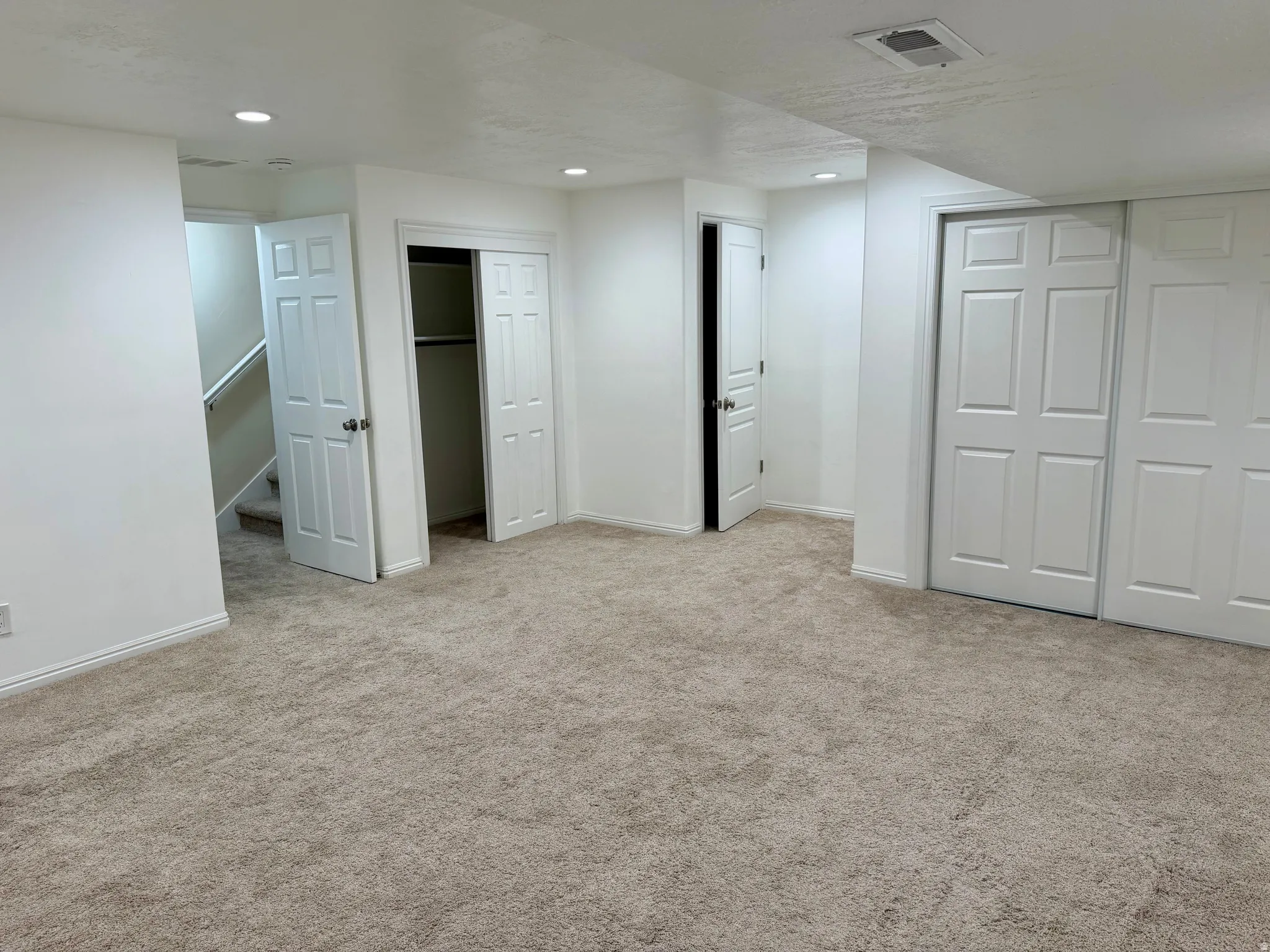 Spacious room featuring neutral carpeting, recessed ceiling lighting, a paneled bifold door closet, a standard paneled door, and white baseboards