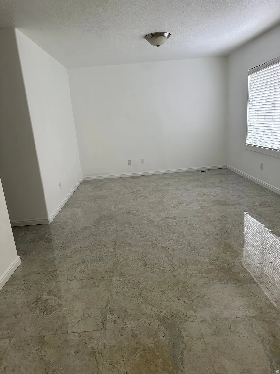 Spacious room featuring neutral tone tile flooring, white baseboards, and a semi-flush mount ceiling light