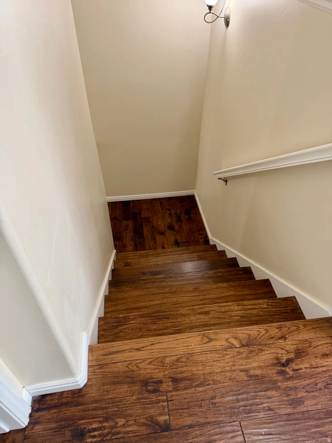 Stairwell featuring wood-finish flooring, light cream wall paint, white baseboards, and a white handrail