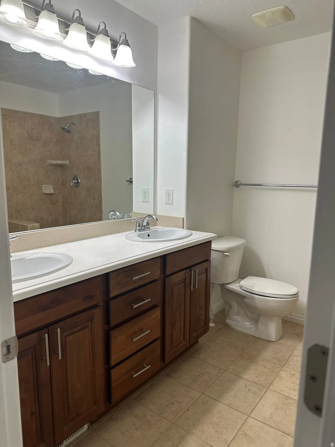 Bathroom featuring a dual-sink vanity with wood-finish cabinetry, a large wall mirror, and a tiled shower enclosure