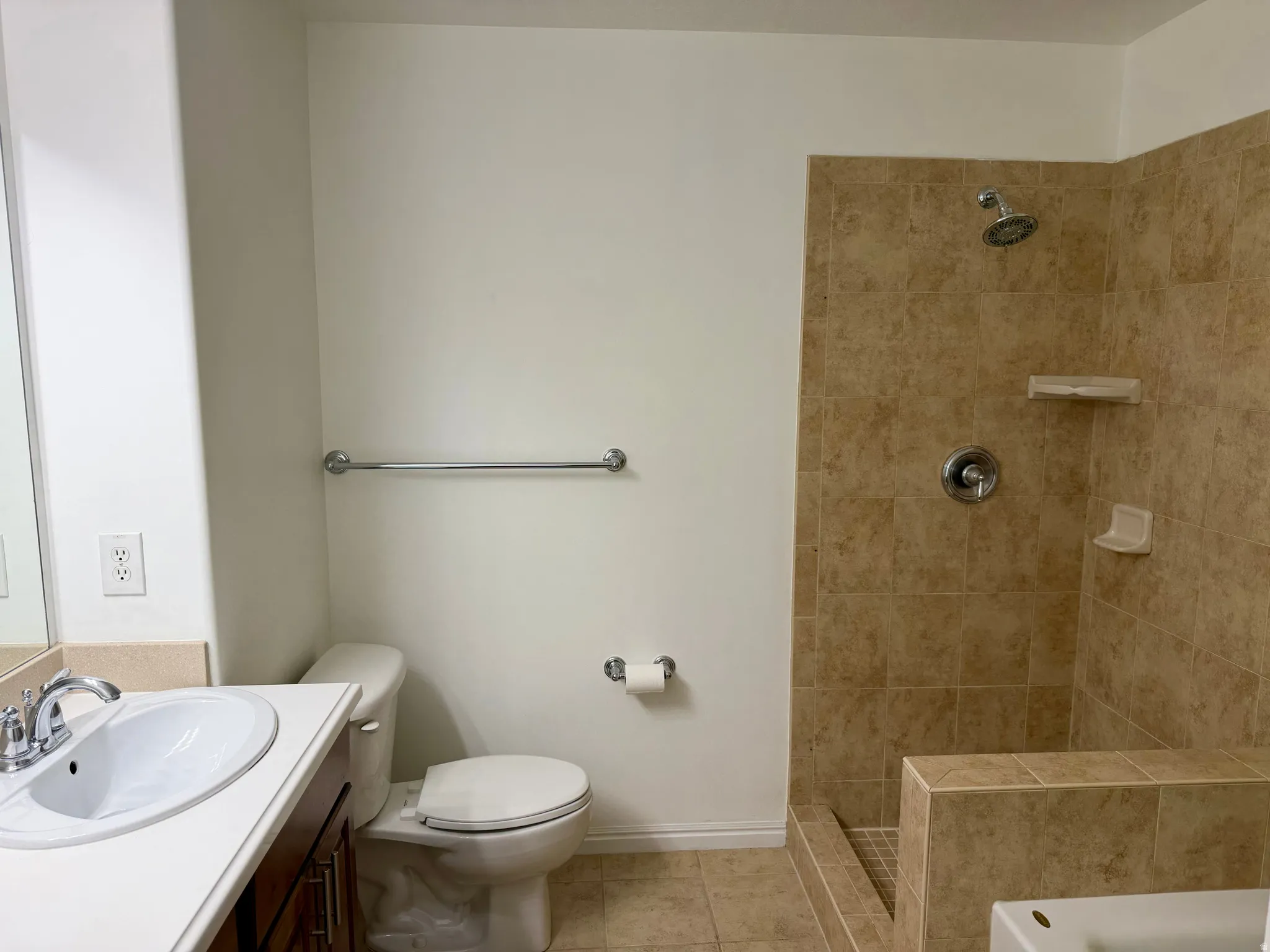 Bathroom featuring a shower with tiled walls and a built-in bench, a white porcelain toilet, and a vanity with a white countertop and integrated sink