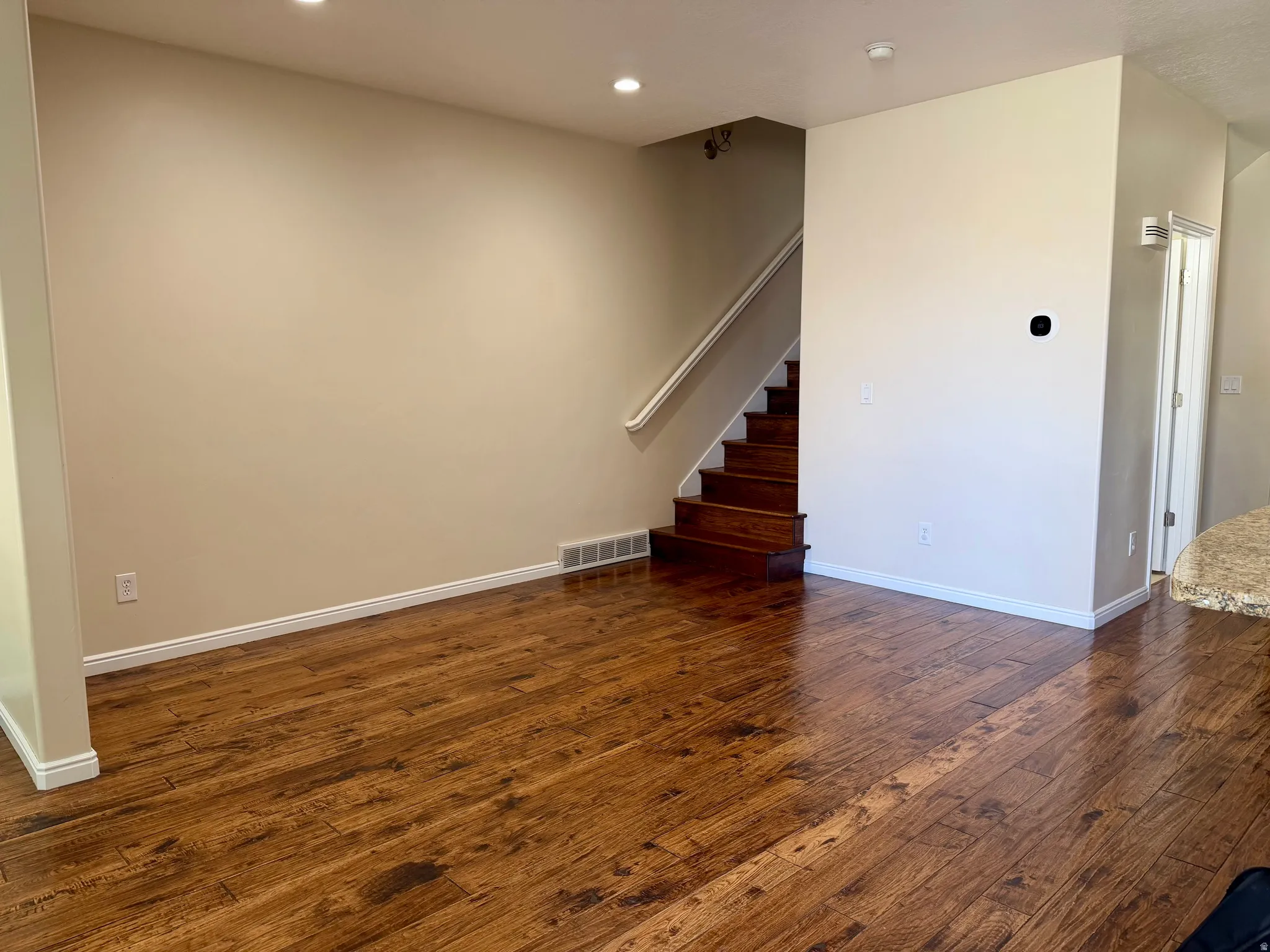 Spacious room featuring wood-finish flooring, recessed ceiling lighting, and a staircase with a white handrail