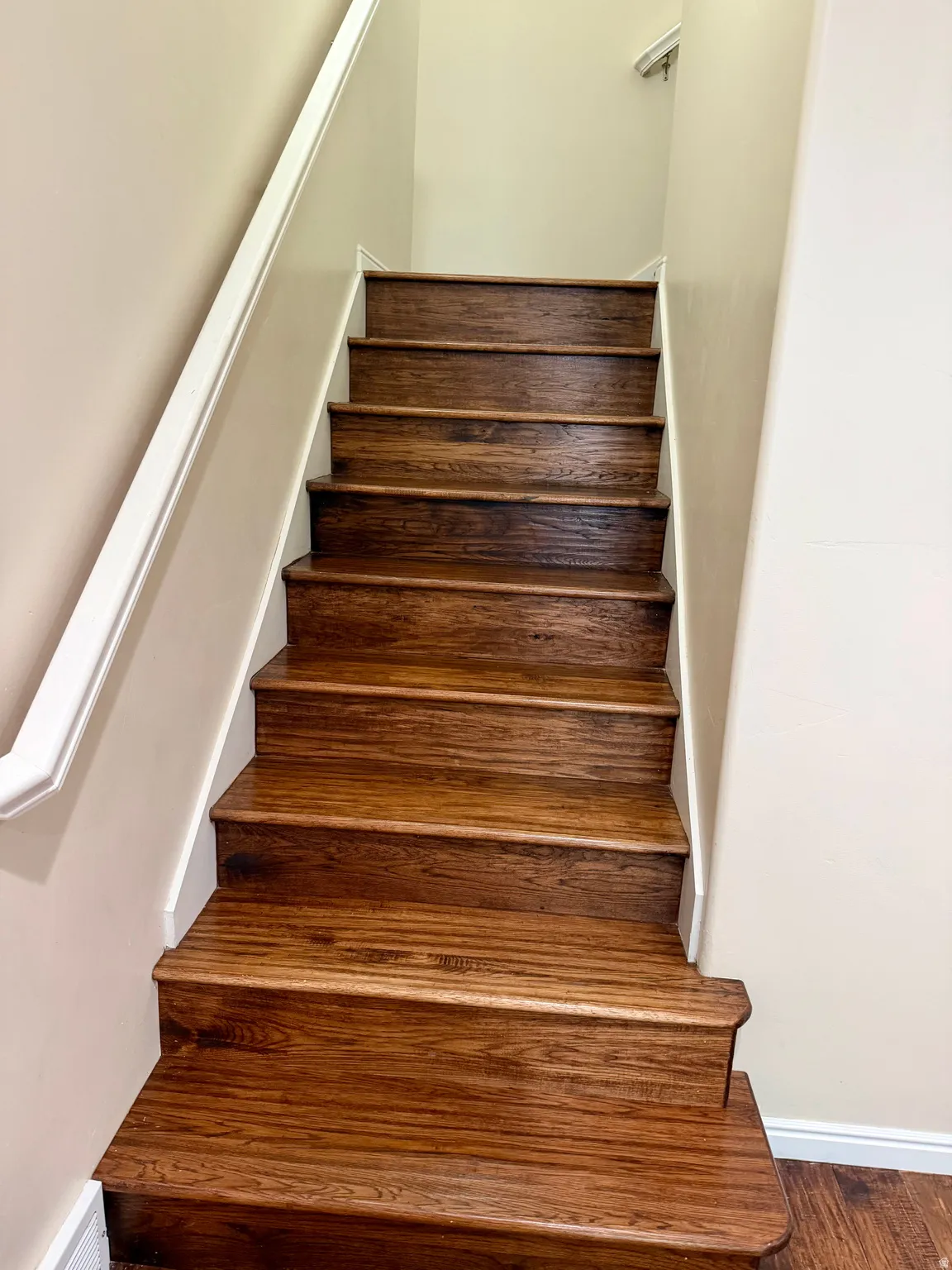 Staircase featuring rich wood-finish treads, white risers, and a contrasting white handrail