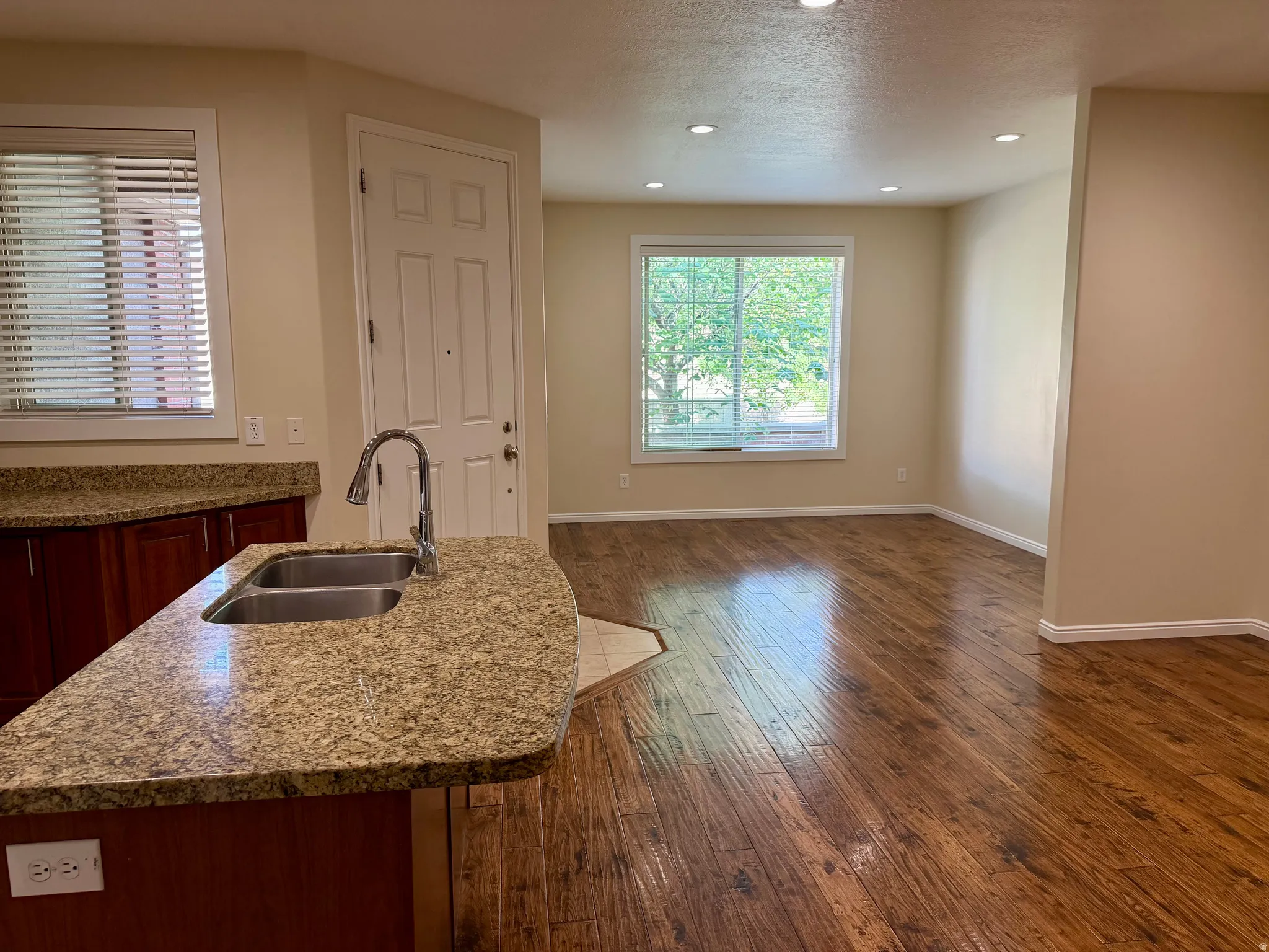 Kitchen island featuring a double-basin stainless steel sink with a high-arc faucet, granite-look countertop, and rich wood-finish cabinetry
