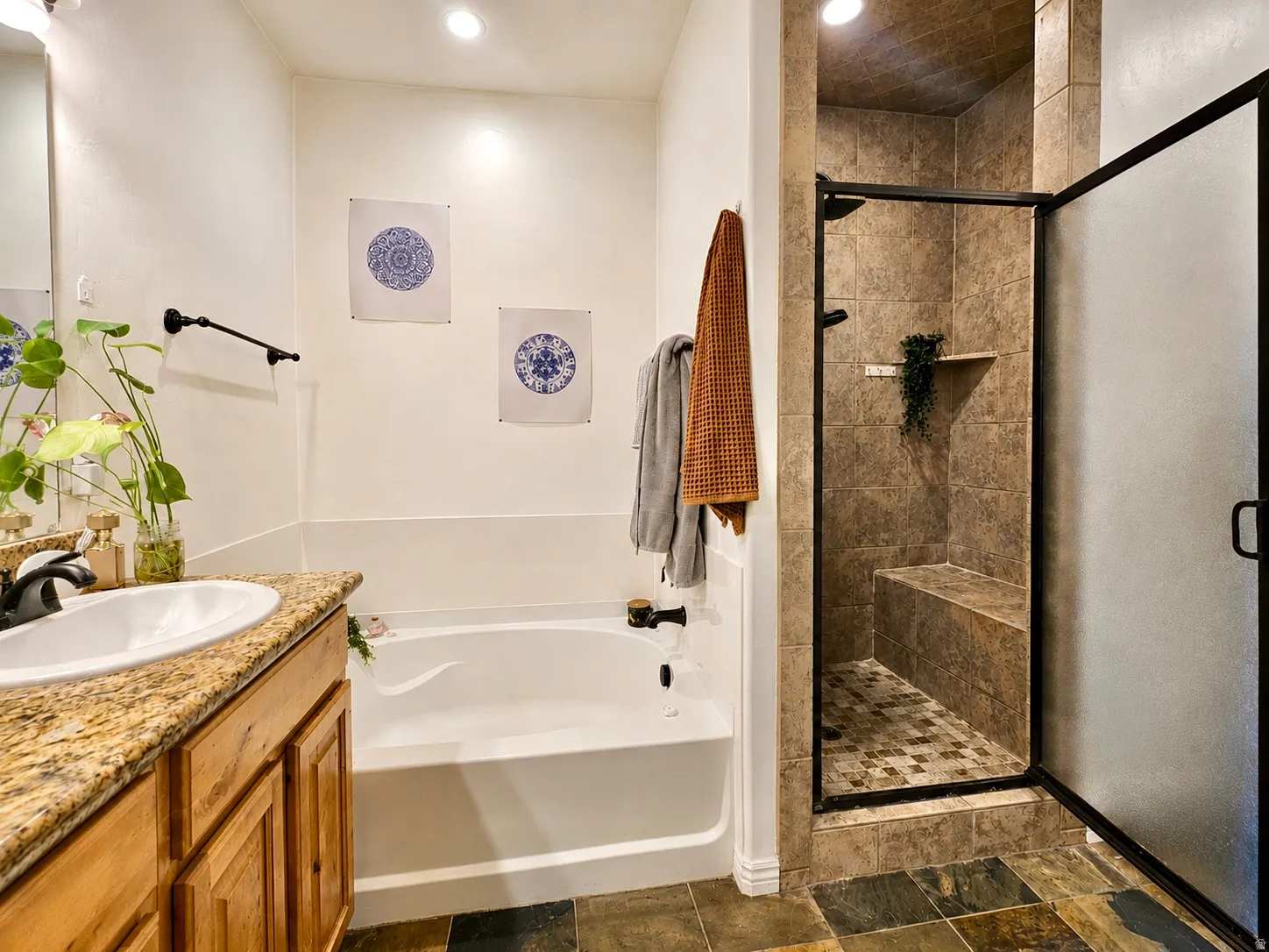 Bathroom featuring a walk-in shower with a built-in bench, a separate soaking tub, a vanity with a granite countertop and wood cabinetry, and slate-style floor tiling