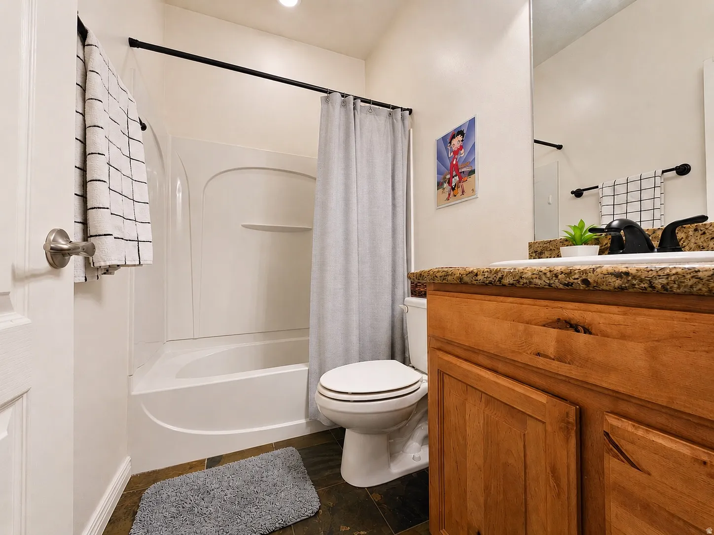 Full bathroom featuring a single vanity with granite-style countertop, wood-finish cabinetry, and a black faucet