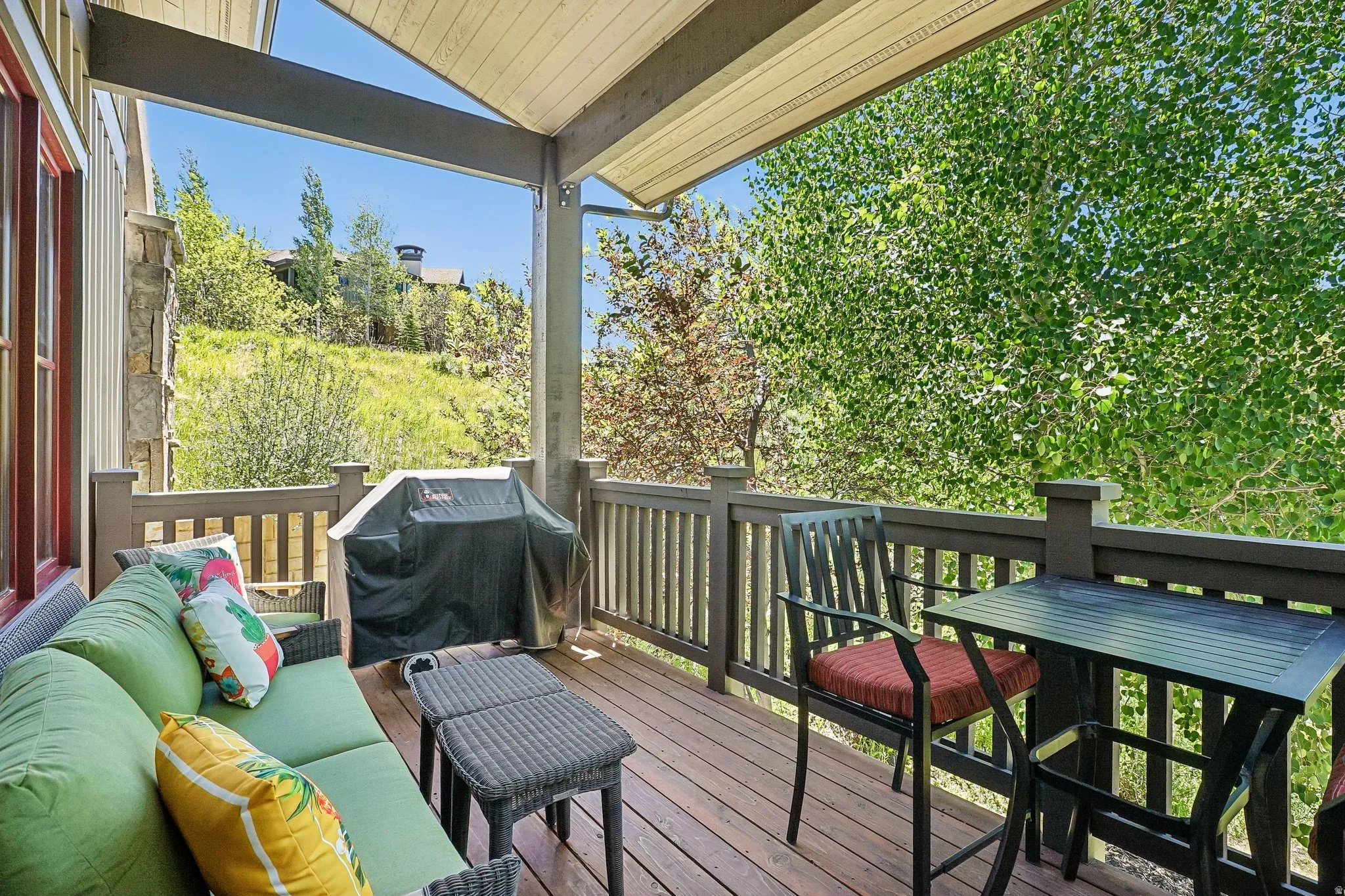 Covered outdoor deck with wood-finish flooring, stone architectural detailing, and a railing system