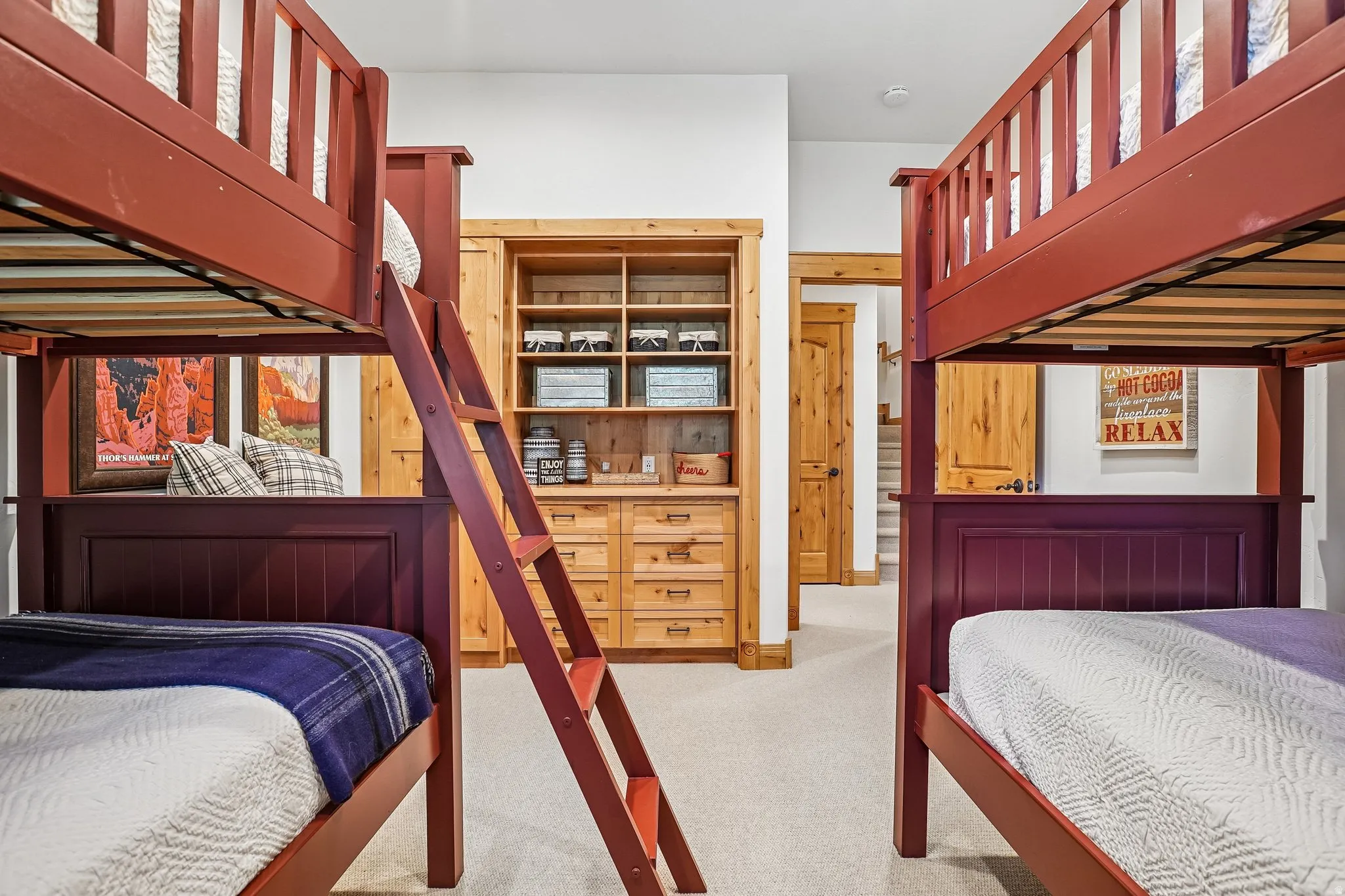 Built-in bunk beds with dark red frames, integrated ladder, natural wood-finish cabinetry with shelving, light neutral carpet, and white walls