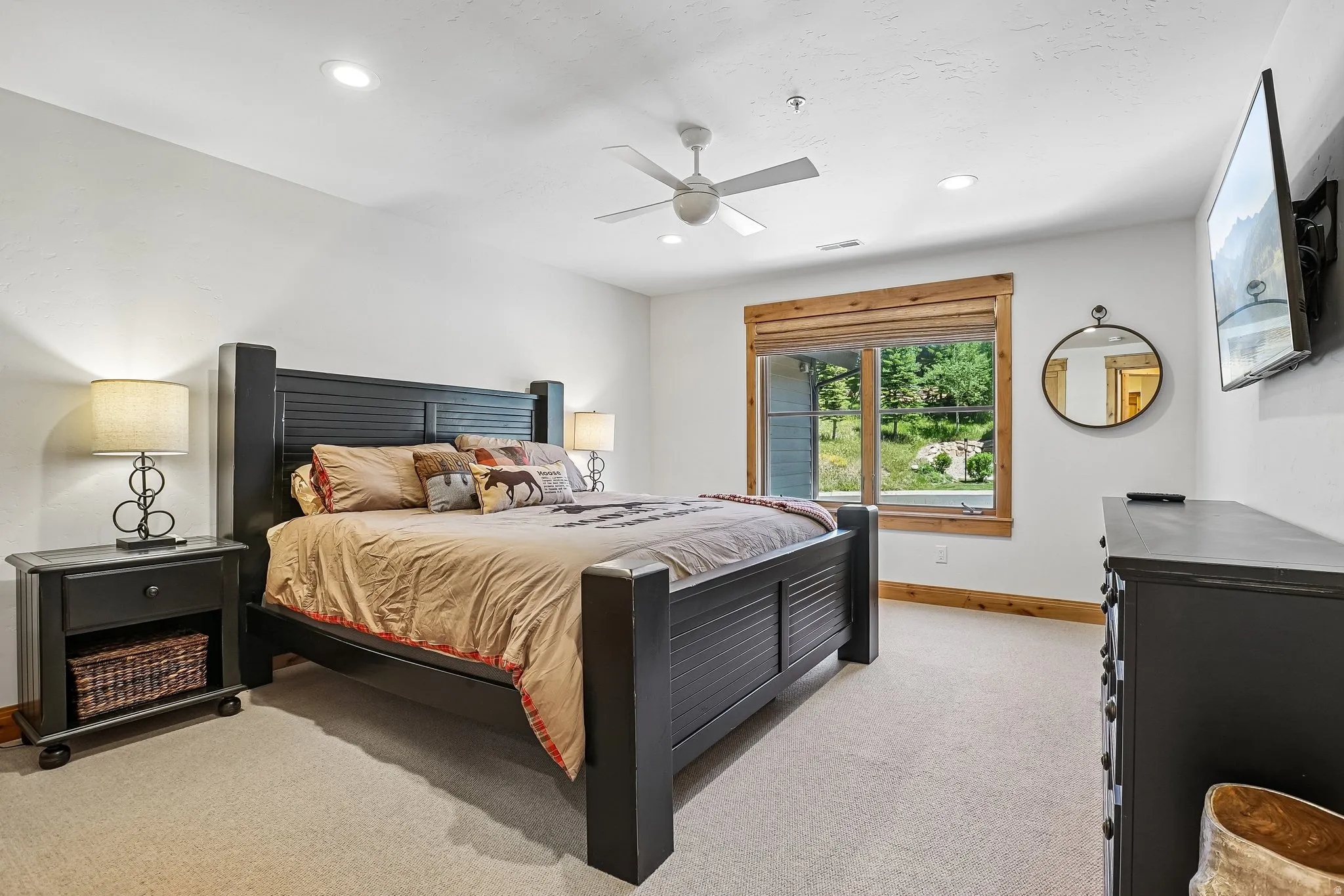 Spacious room featuring carpeted flooring, a ceiling fan, recessed lighting, a large window with natural wood trim, and a wall-mounted mirror