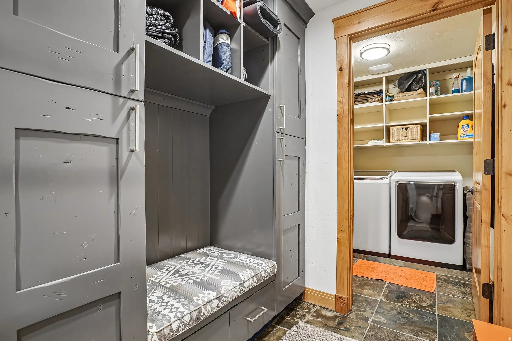 Built-in entryway storage with shelving and seating, accompanied by a dedicated laundry area featuring a washer, dryer, and extensive open shelving