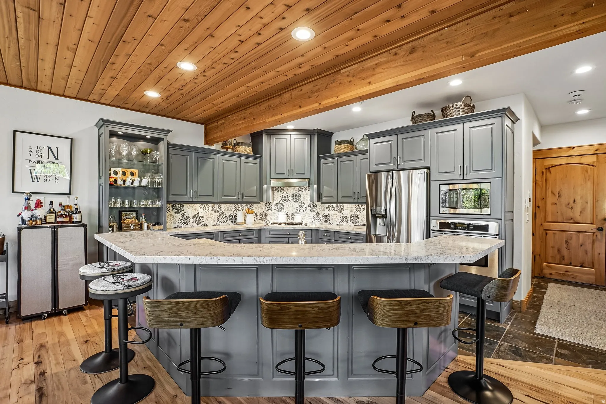 Kitchen featuring a U-shaped island with seating, grey cabinetry, stainless steel appliances, and a wood-paneled ceiling with recessed lighting