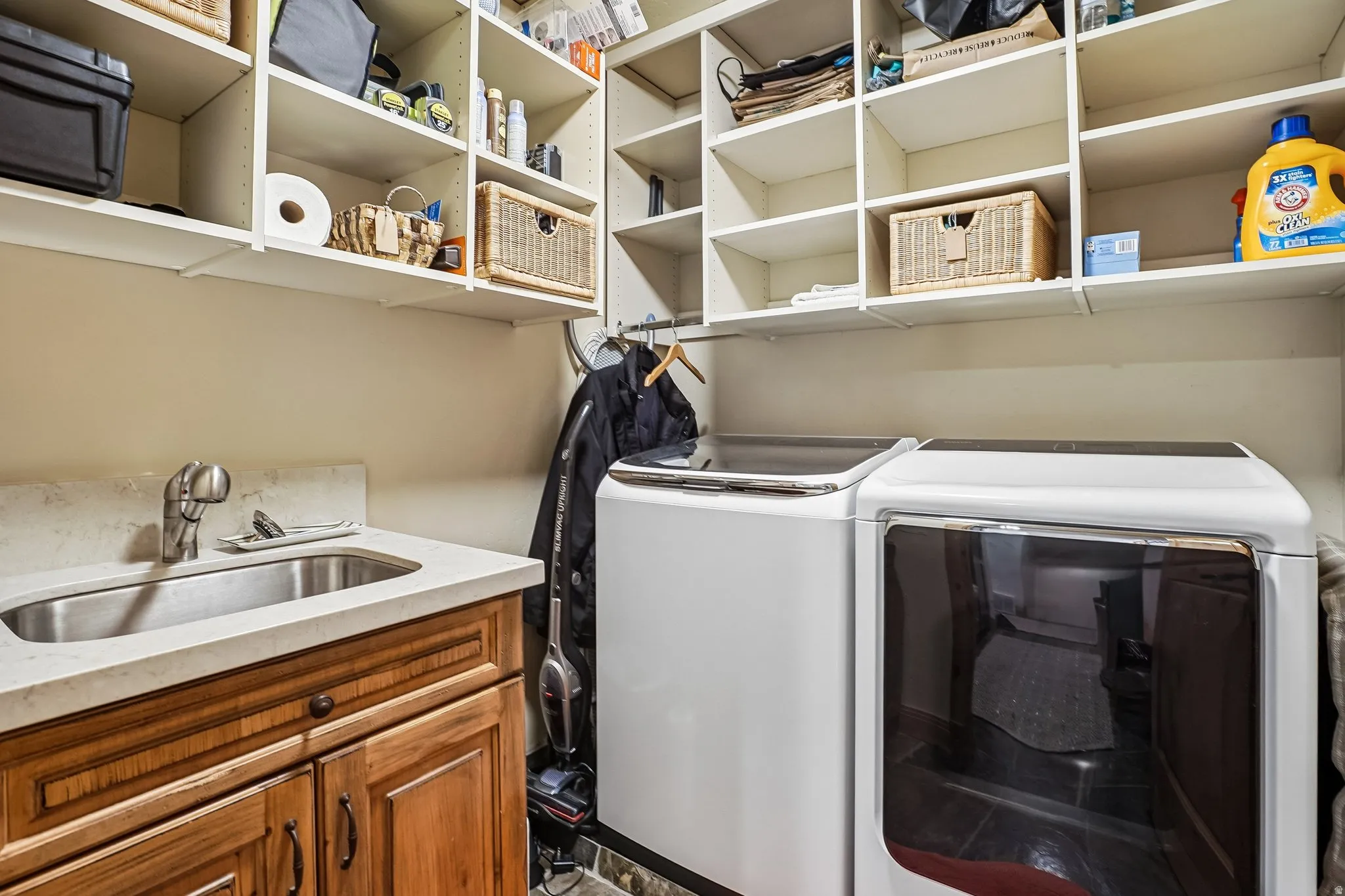 Laundry area featuring built-in shelving, a utility sink with a stone-finish countertop, wood-finish cabinetry, and dark-toned flooring