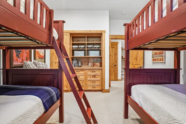Built-in bunk beds with dark red frames, integrated ladder, natural wood-finish cabinetry with shelving, light neutral carpet, and white walls