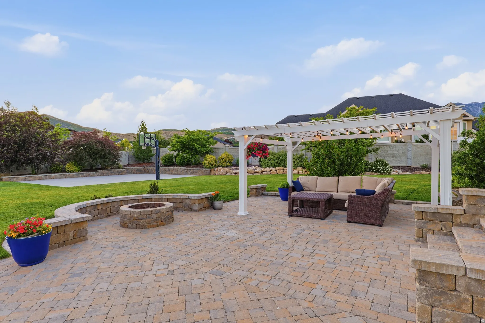 Paver patio featuring a built-in stone fire pit and a white pergola with string lighting