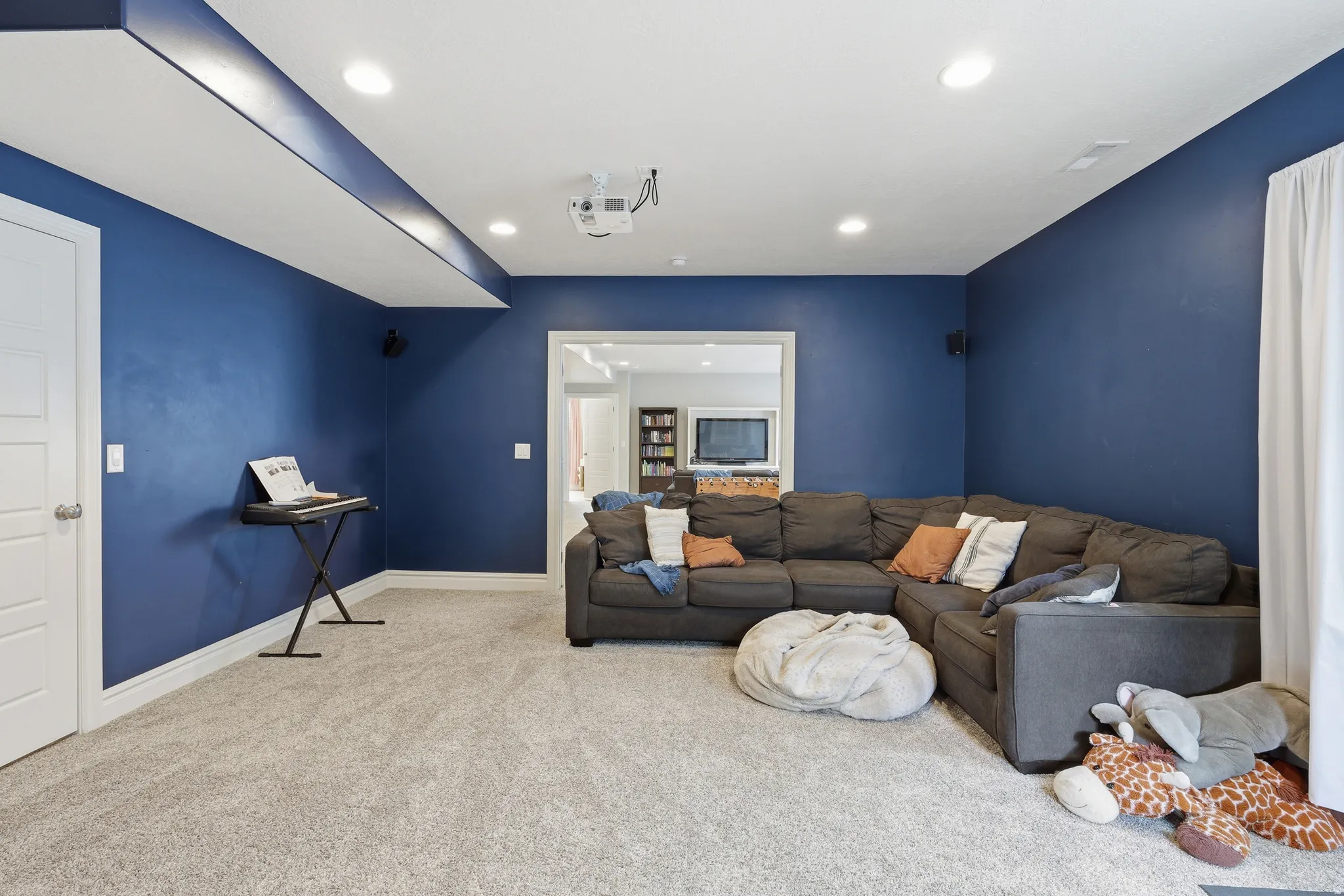 Carpeted entertainment area featuring recessed lighting, a built-in ceiling projector, and a wide entryway