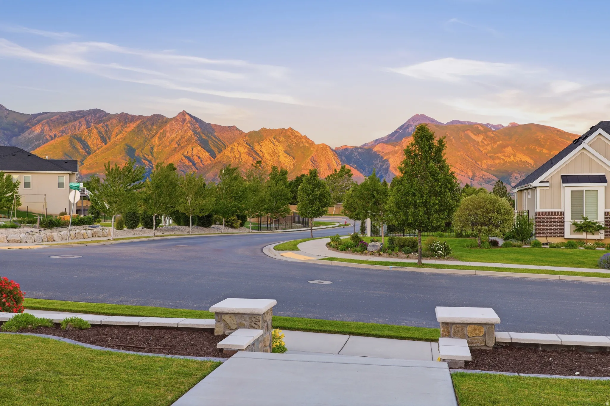 Sweeping mountain backdrop frames a residential street with landscaped lawns and mature trees