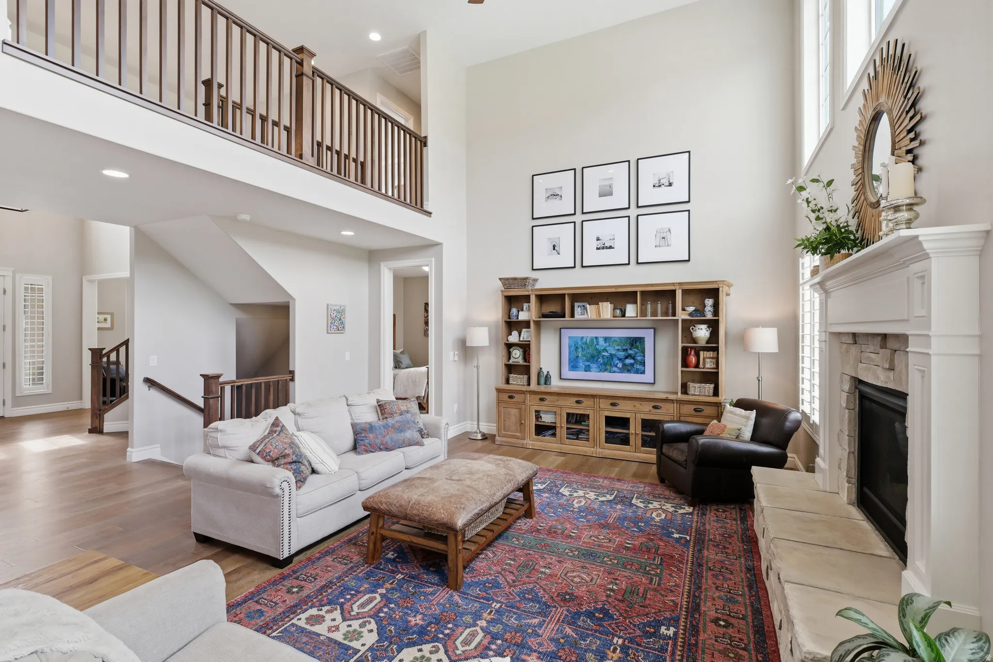 Two-story living area featuring high ceilings, a built-in media center, a stone-surround fireplace with a classic mantel, and wood-finish flooring