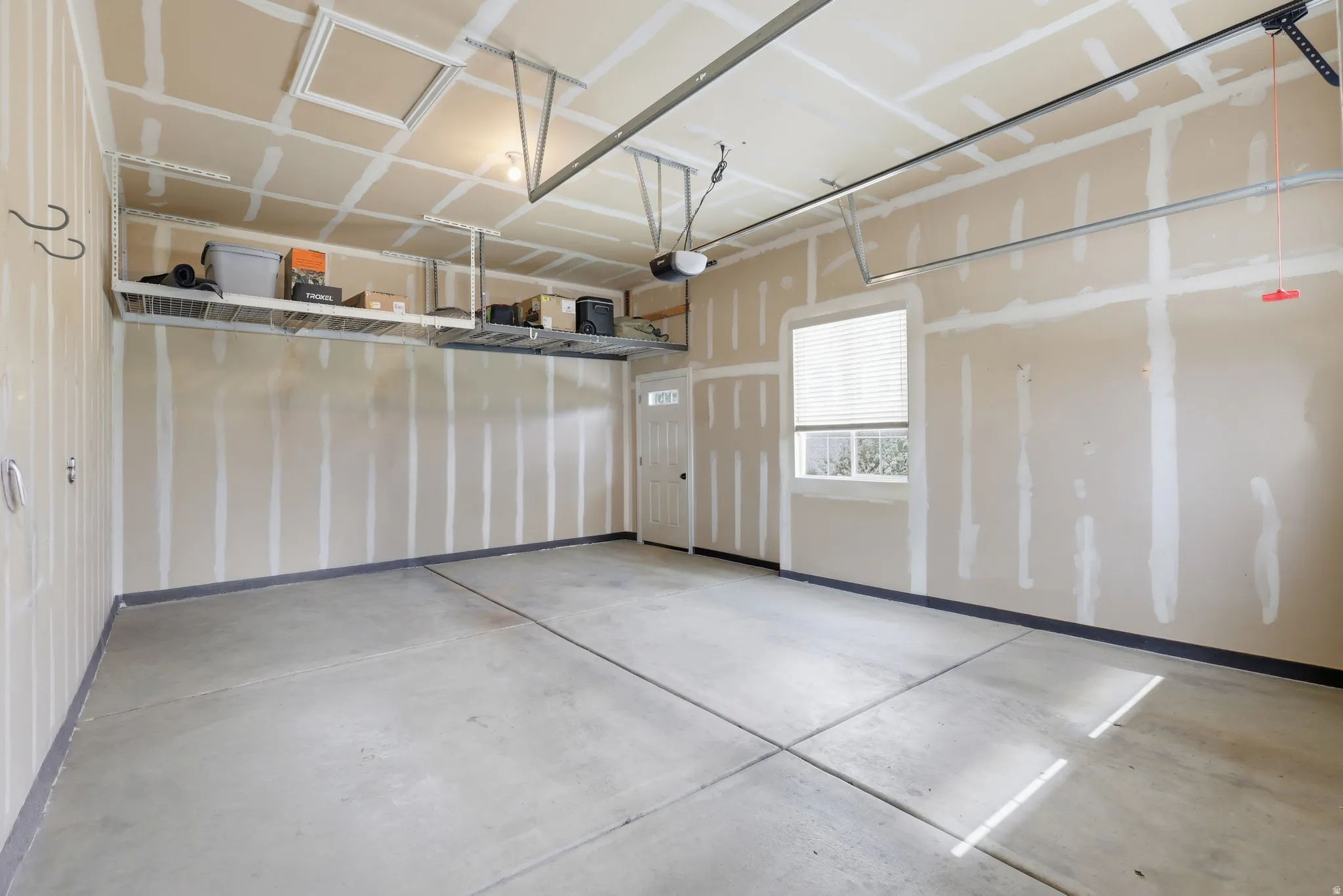 Spacious garage featuring a concrete floor, overhead storage racks, an automatic garage door opener, and a window with blinds