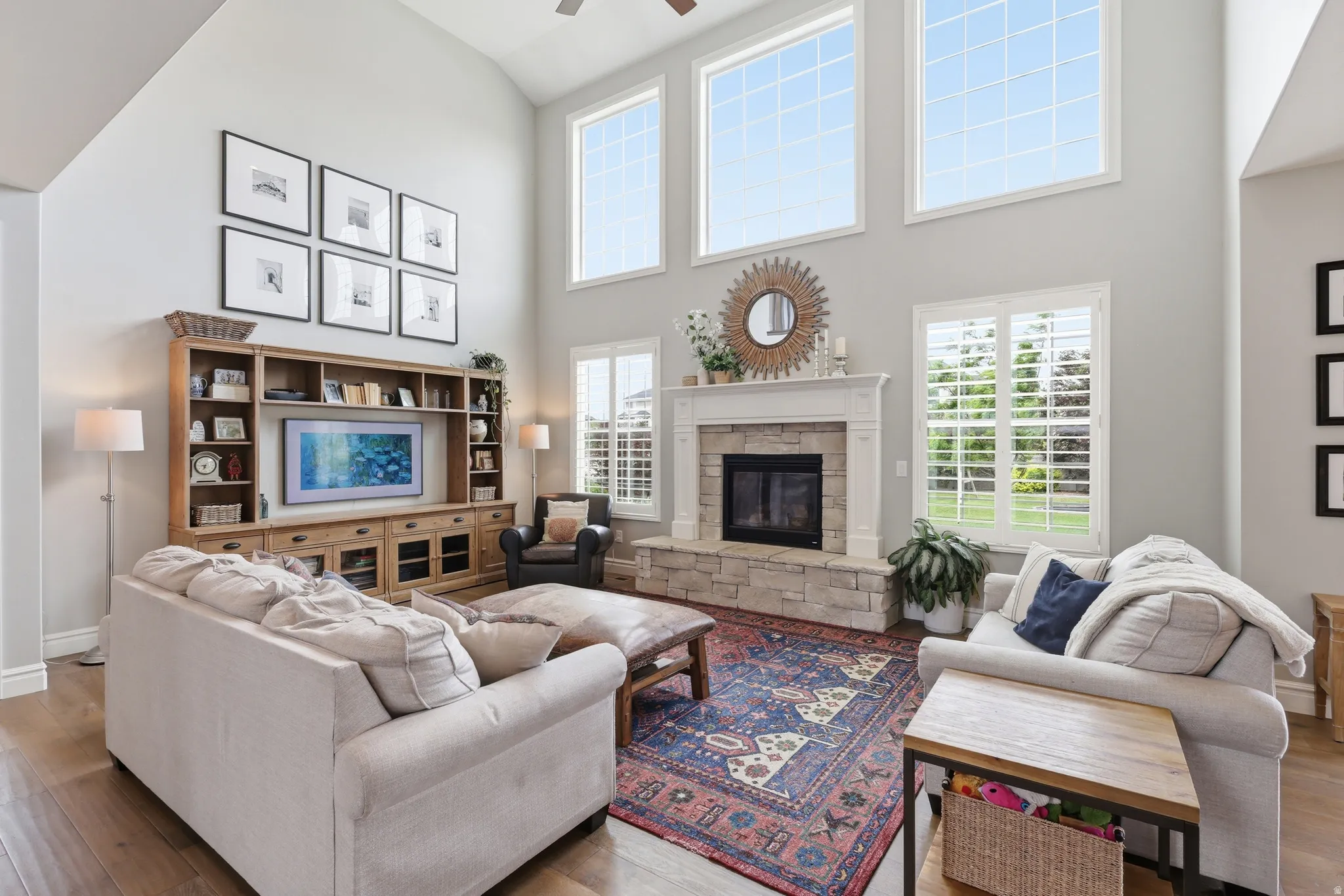 Living area featuring a stone surround fireplace with a mantel, tall vaulted ceilings, and wood-finish flooring