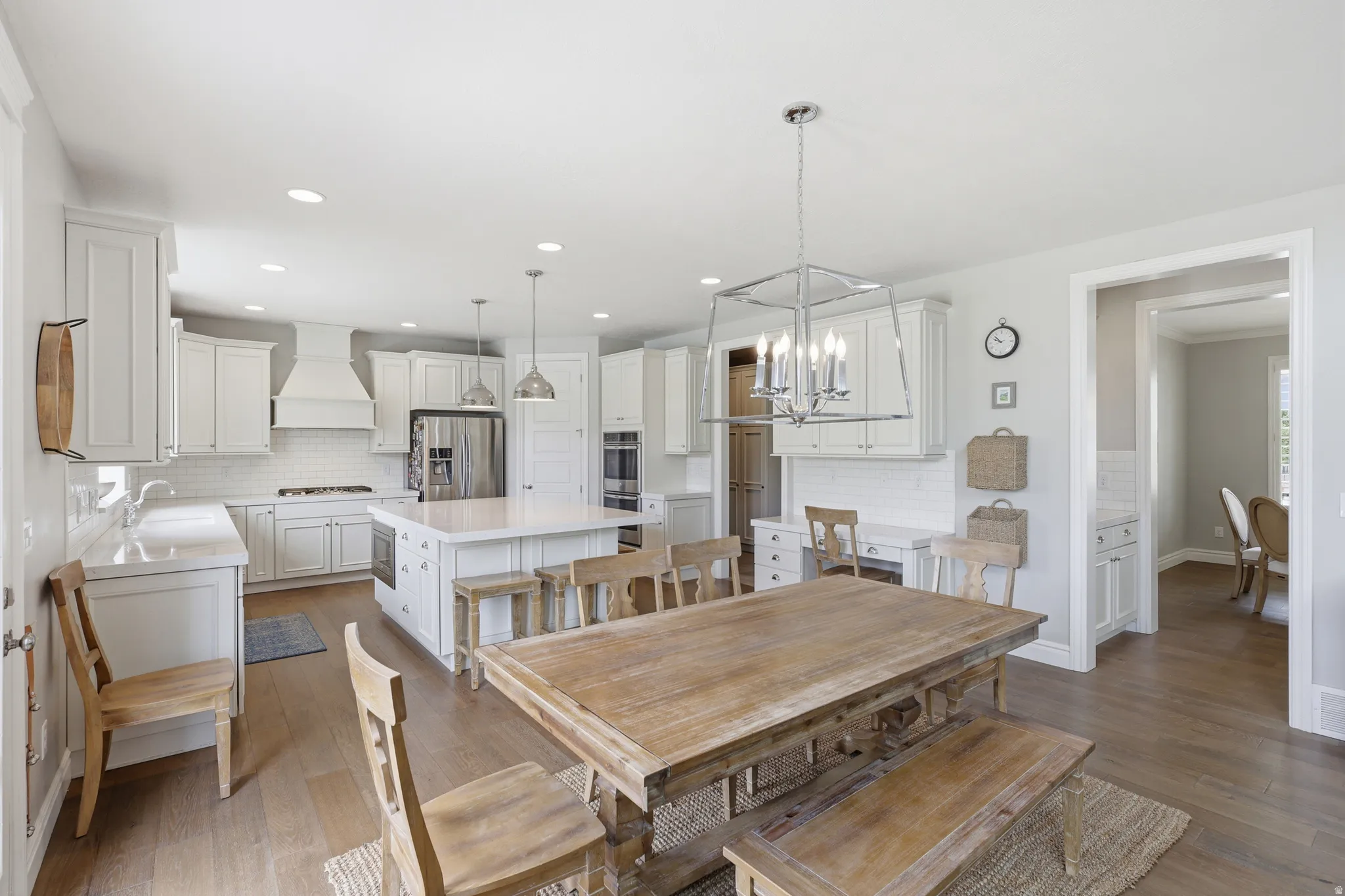Bright open-concept kitchen featuring white shaker cabinetry, stainless steel appliances, a center island with seating, a subway tile backsplash, and wood-finish flooring