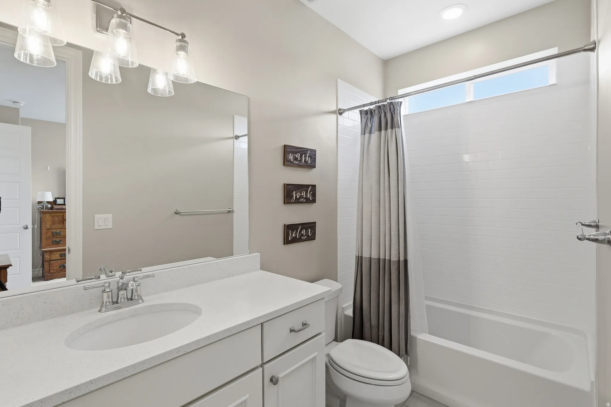 Bathroom featuring a white vanity with an undermount sink, a large mirror, a built-in bathtub with subway tile surround, and a clerestory window