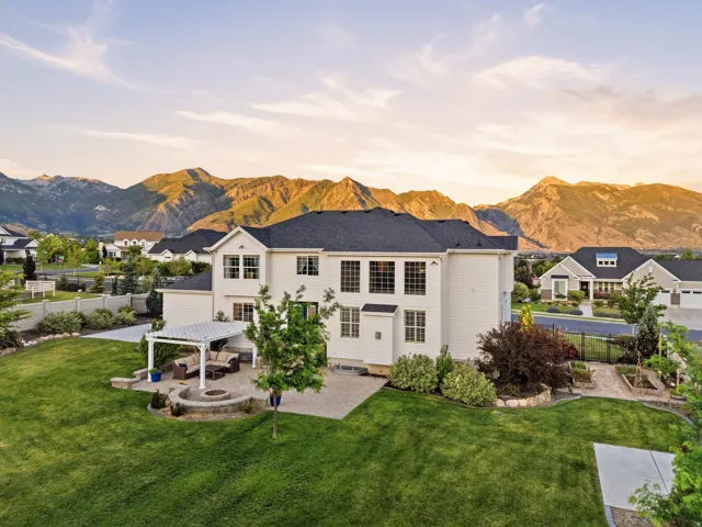 Expansive backyard featuring a paver patio with pergola, built-in fire pit, manicured lawn, and mature landscaping