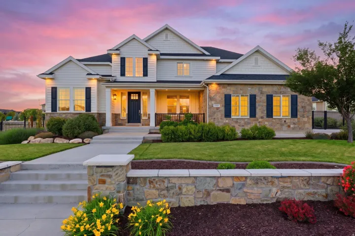 Distinguished two-story residence featuring a combination of stone and siding exterior, black shutters, and a covered porch