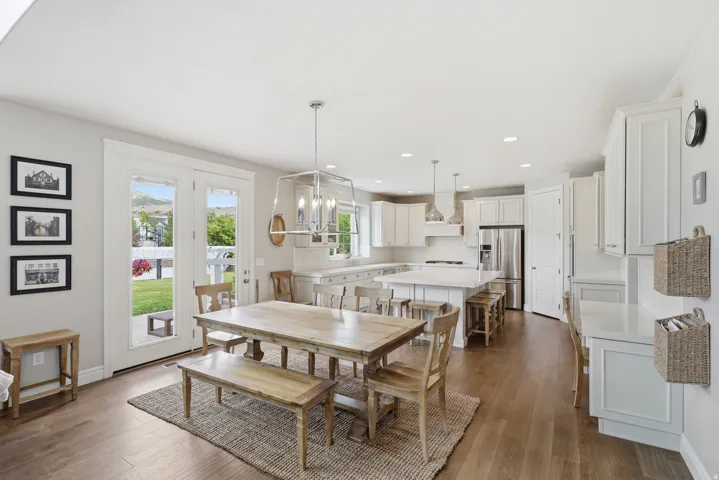 Open-concept kitchen and dining area featuring light-finish wood flooring, white shaker cabinetry, stainless steel appliances, and a central island with seating