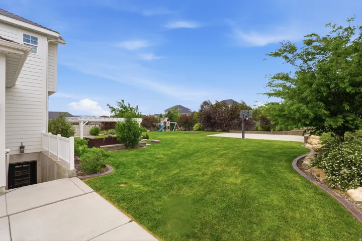 Expansive green lawn featuring a concrete sport court with a basketball hoop, a white vinyl fence, and a white pergola