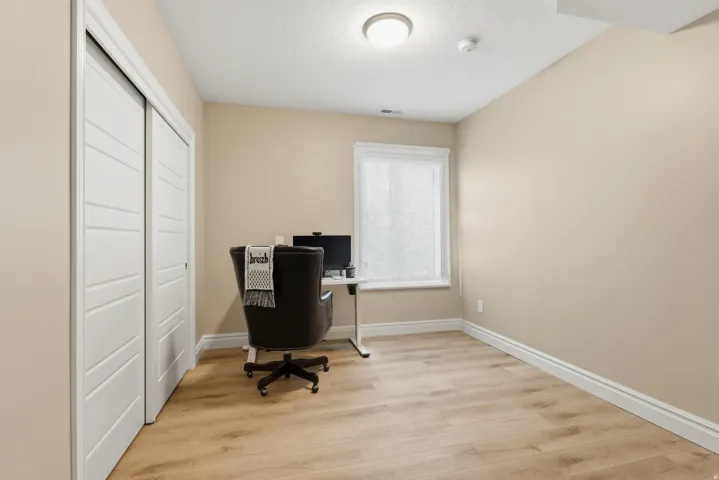 Neutral-toned interior room with wood-finish flooring, a single window with white trim, and a built-in closet with bifold doors