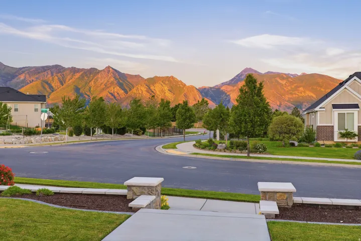 Sweeping mountain backdrop frames a residential street with landscaped lawns and mature trees
