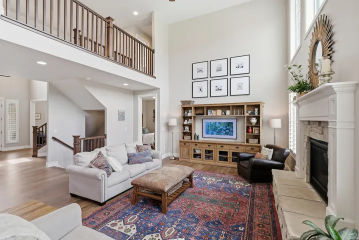 Two-story living area featuring high ceilings, a built-in media center, a stone-surround fireplace with a classic mantel, and wood-finish flooring