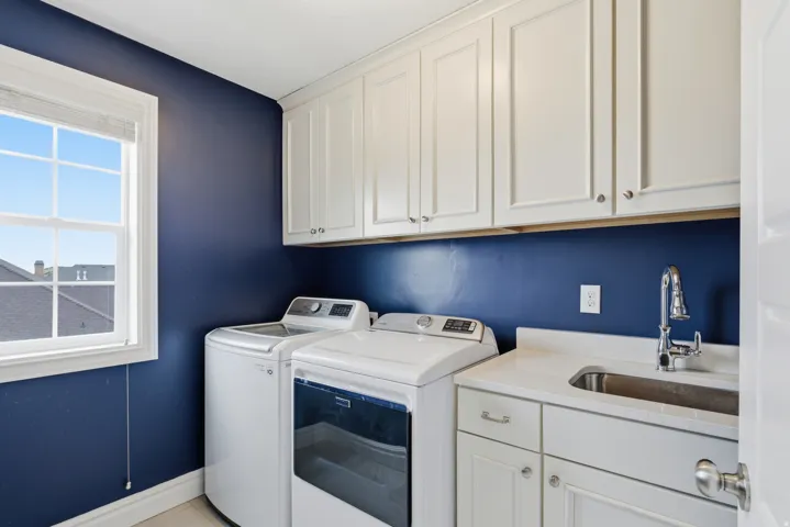 Laundry room featuring white shaker-style cabinetry, a built-in sink with a gooseneck faucet, a light-toned countertop, and a window for natural illumination