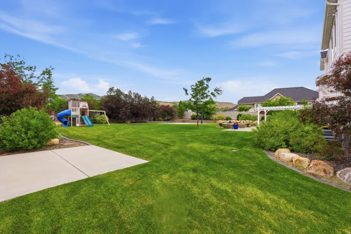 Expansive green lawn with a concrete patio, mature trees, and landscaping boulders