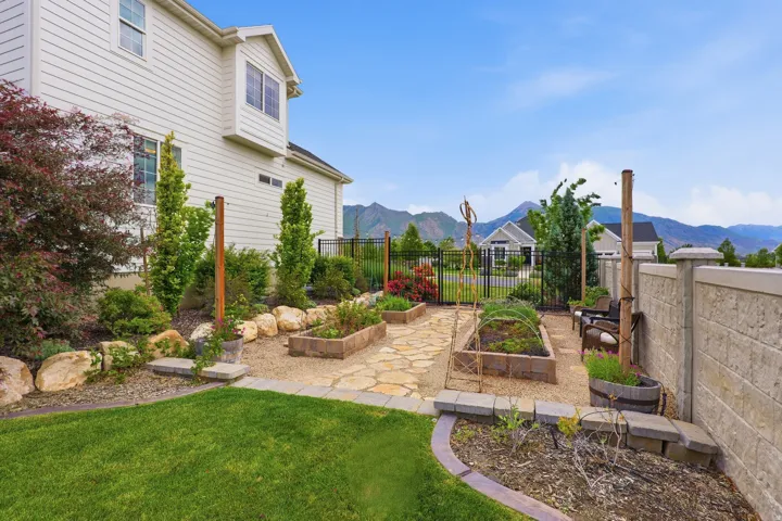 Landscaped backyard featuring a stone pathway, raised garden beds, a gravel area, and a privacy wall