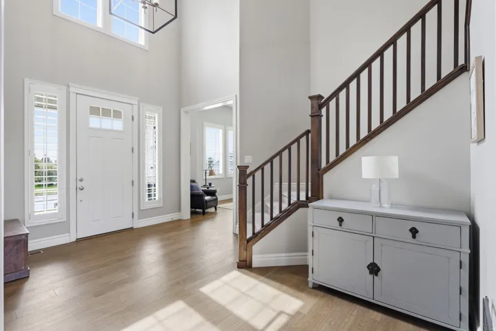 Two-story entryway featuring wood-finish flooring, a white paneled front door with multiple glass panes, and sidelight windows