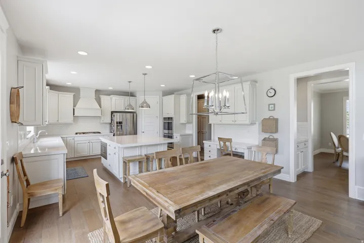 Bright open-concept kitchen featuring white shaker cabinetry, stainless steel appliances, a center island with seating, a subway tile backsplash, and wood-finish flooring