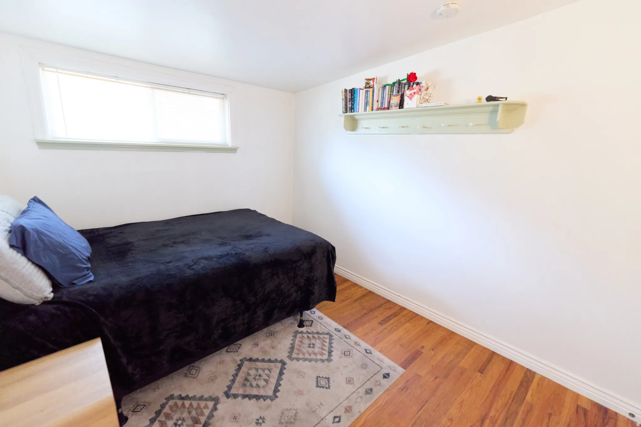 Room featuring wood-finish flooring, a built-in wall shelf, a rectangular window, and white trim