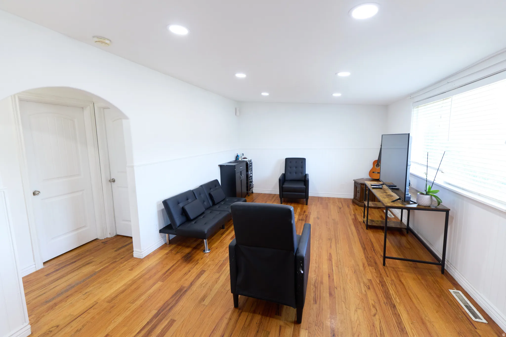 Spacious room featuring rich wood-finish flooring, recessed lighting, and a prominent window with horizontal blinds