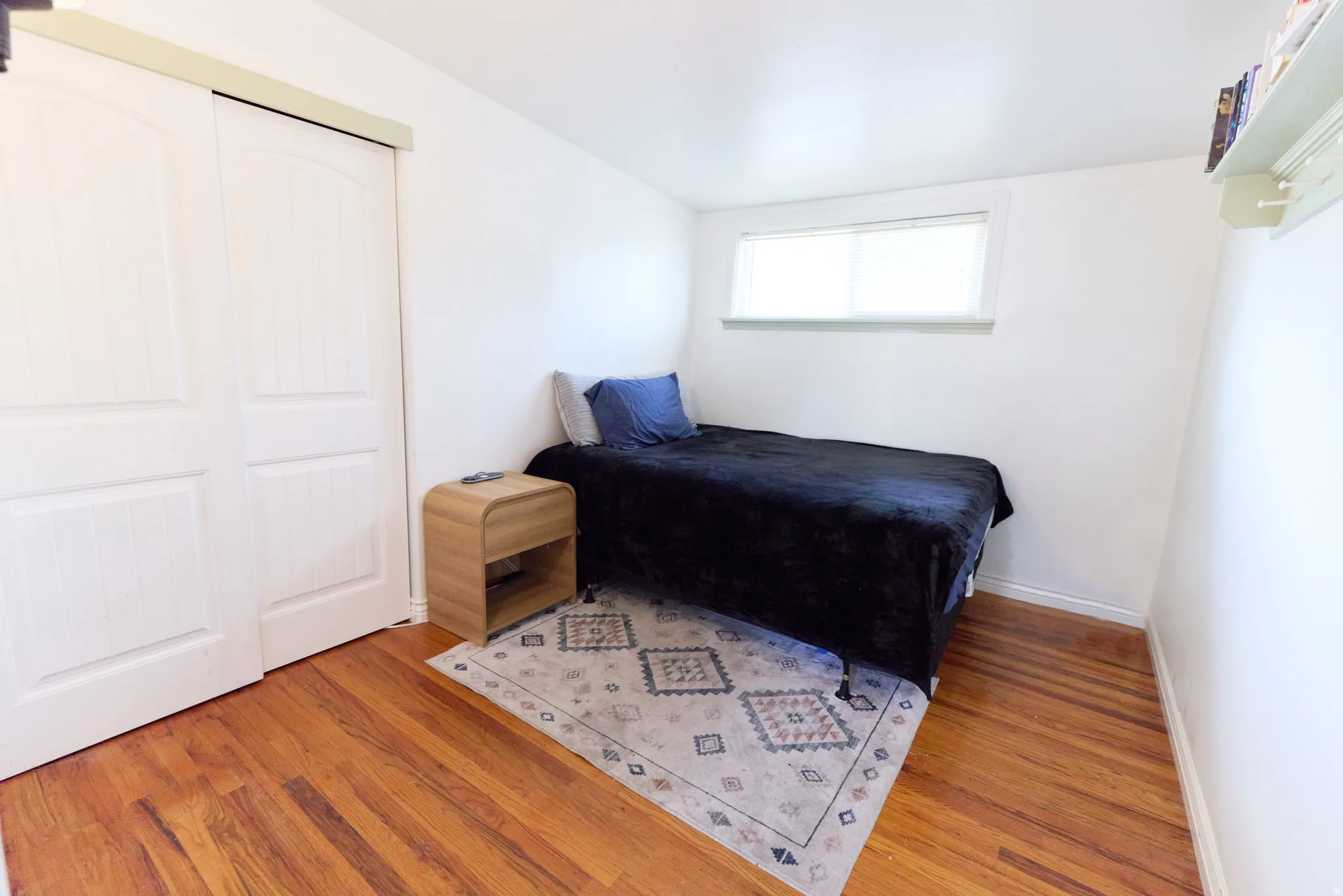 Bedroom with wood-finish flooring, a double-door closet, white walls, and a window providing natural light